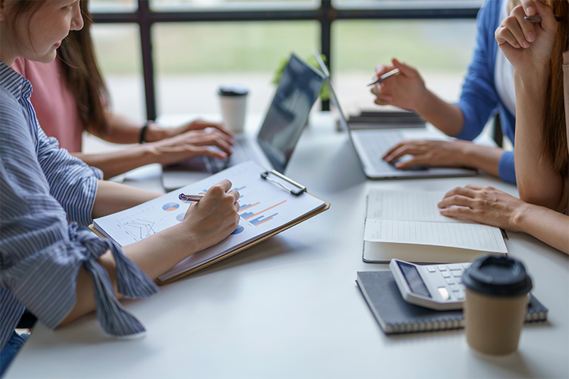 Accountants collaborating at a conference table with laptops, calculators, and coffee.